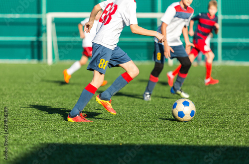 football teams - boys in red, blue, white sportswear play soccer on the green field. boys dribbling. dribbling skills. Team game, training, active lifestyle, hobby, sport for kids concept © Natali