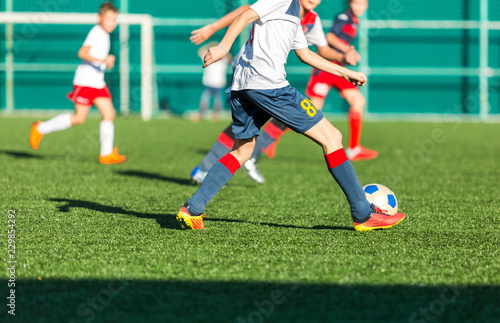 football teams - boys in red, blue, white sportswear play soccer on the green field. boys dribbling. dribbling skills. Team game, training, active lifestyle, hobby, sport for kids concept © Natali