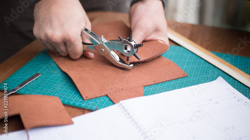 Tanners hands at work with revolver punch and leather. Selected focus, close up.