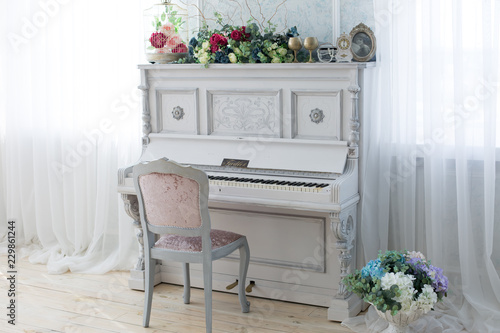 white piano. a piano and a chair. the piano is decorated with flowers. piano by the window