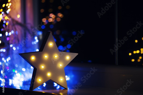 Glowing white LED star near window on warm bokeh background indoor at night.