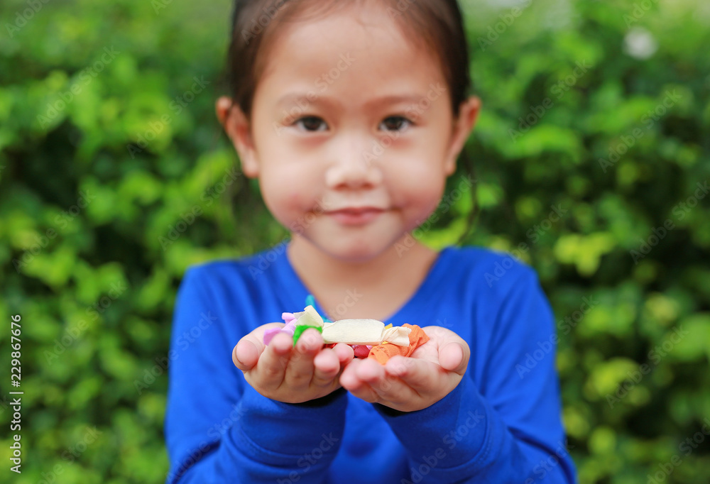 Asian child girl holding some thai sugar and fruit toffee with colorful paper wrapped in her hands. Focus at candy in her hands. Asian child girl holding some thai sugar and fruit toffee with colorful paper wrapped in her hands. Focus at candy in her hands.