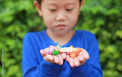 Close-up little Asian child girl holding some thai sugar and fruit toffee with colorful paper wrapped in her hands.