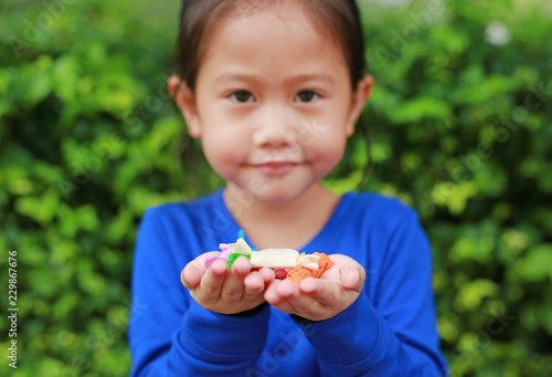 Asian child girl holding some thai sugar and fruit toffee with colorful paper wrapped in her hands. Focus at candy in her hands.
