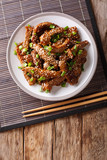 Traditional Asian beef teriyaki with green onions and sesame close-up on a plate. Vertical top view