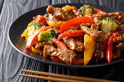 delicious Asian teriyaki beef with red and yellow bell peppers, broccoli and sesame seeds close-up on a plate. horizontal