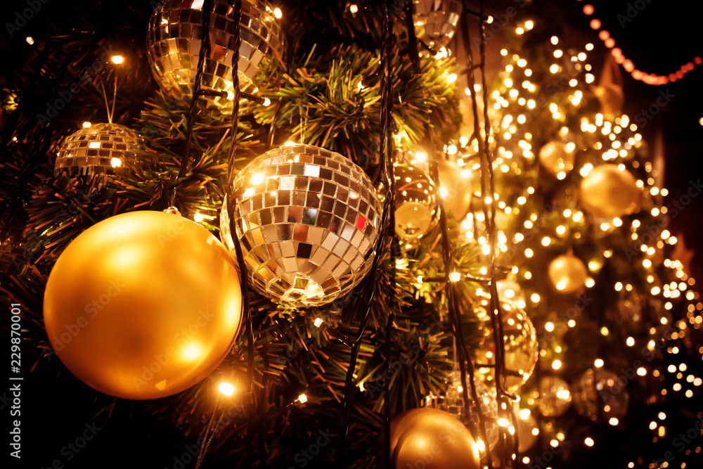 Christmas tree with gold ball and bokeh lights background. Xmas abstract close up with glowing decorations outdoors.