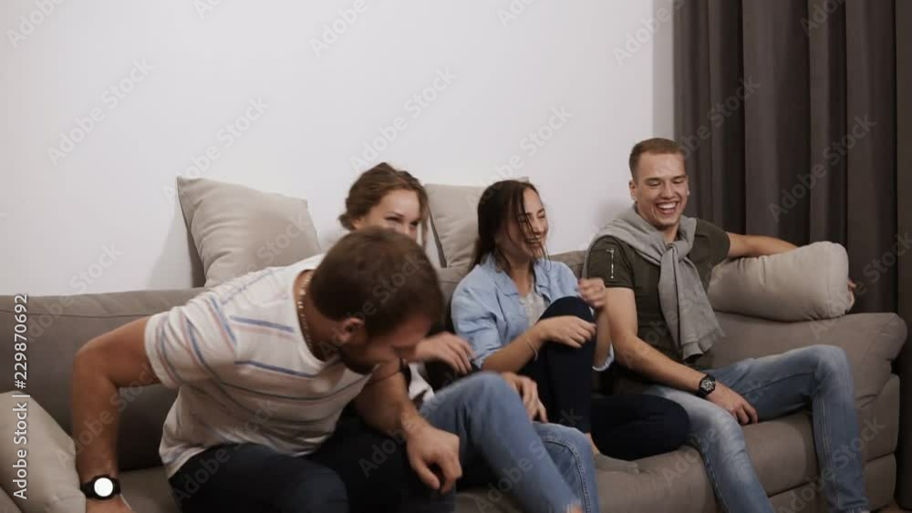Group of four came to a small living room and sitting on grey sofa, laughing, having fun time together. Friendship, communication, party time concept Group of four came to a small living room and sitting on grey sofa, laughing, having fun time together. Friendship, communication, party time concept