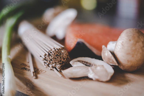 udon noodles, spring onion, mushrooms and salmon on a wooden board in the kitchen