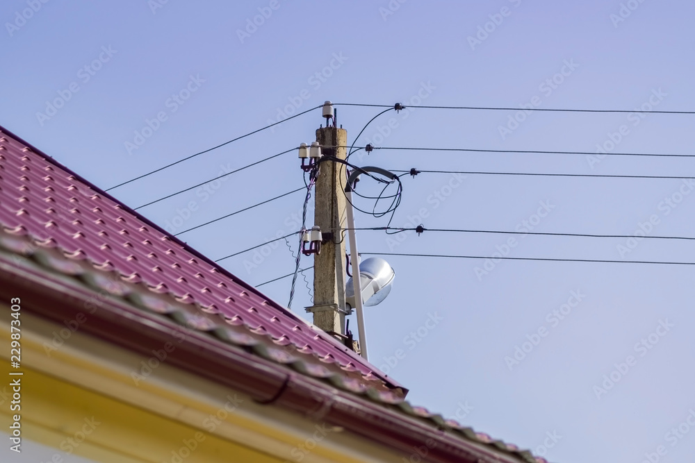 Electric pole and red tile roof on blue sky background. Power supply in countryside. Electric pole and red tile roof on blue sky background. Power supply in countryside.