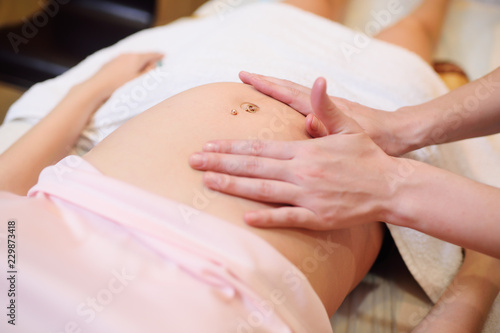 the massage therapist makes a belly massage to a pregnant young woman