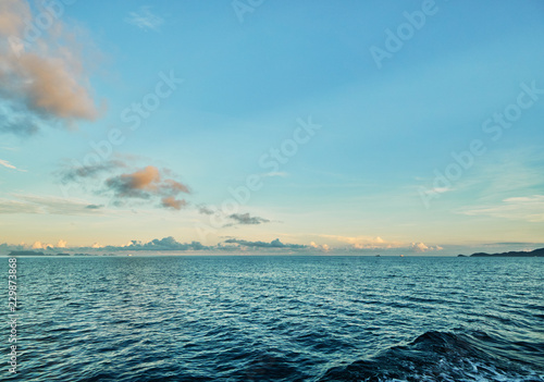  View from the yacht at the ocean on the background of the blue sky and sun rising over island