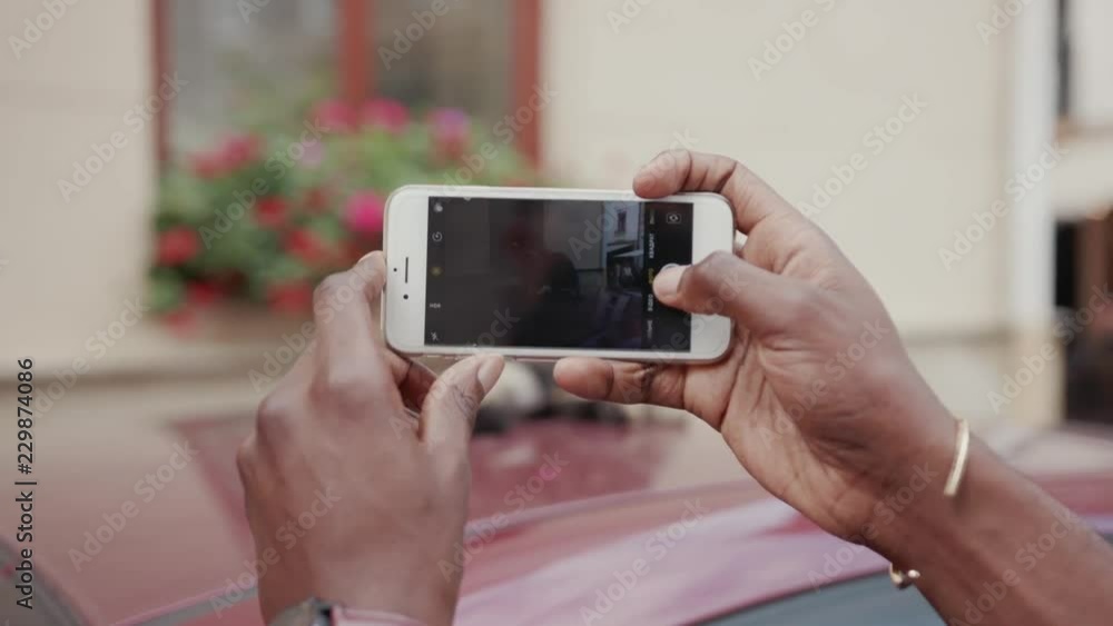Hands of young African man holding smartphone. Guy taking pictures of cute cat laying on automobile. Parts of body. Summertime. Outdoors. Hands of young African man holding smartphone. Guy taking pictures of cute cat laying on automobile. Parts of body. Summertime. Outdoors.