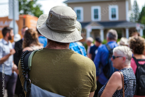 Man with a hat is listening to a public speech given in front of 100 people - Shot from the back during an alternative political gathering