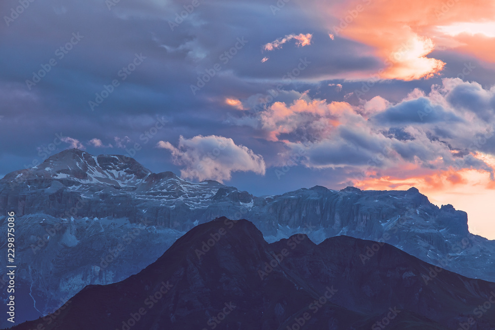 Beautiful mountain peaks covered by colored clouds at sunset, mountain landscape background
