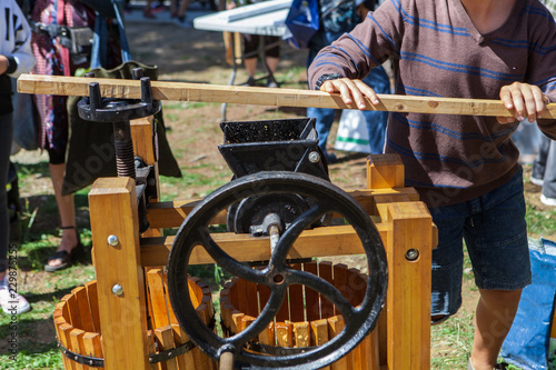 Young man is making apple juice using the big lever of an old fashion apple press, as part of a community workshop - Closeup picture with people in the background
