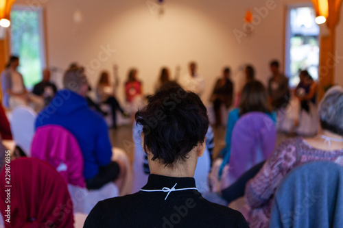 Young woman with black hair and black jacket is listening to a conference given by multiple specialists - Pictured from the back in an alternative health center photo