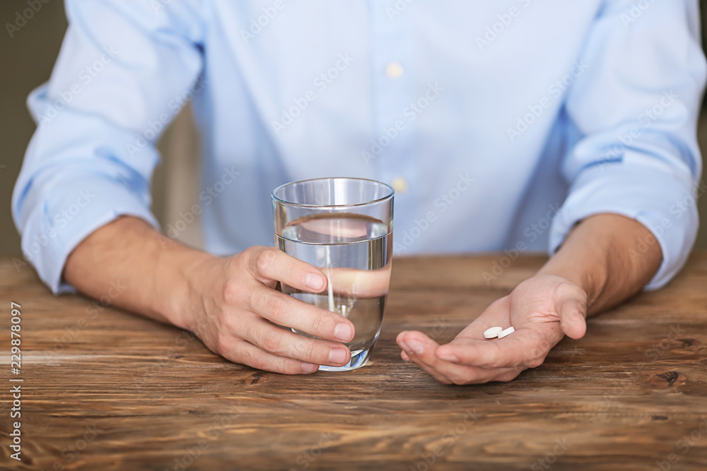 Man holding pills and glass of water at wooden table, closeup