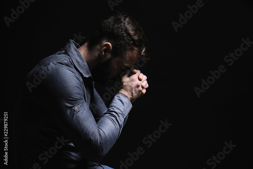 Obraz na plátně Religious young man praying to God on black background