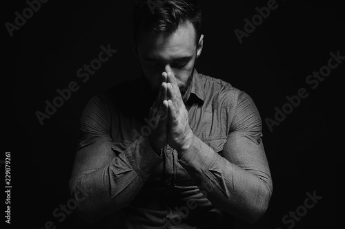 Religious young man praying to God on dark background, black and white effect