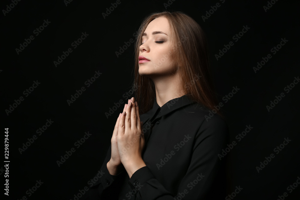 Beautiful young woman praying on dark background Beautiful young woman praying on dark background