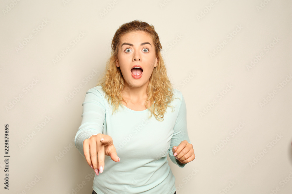 Portrait of shocked young woman pointing at viewer on light background Portrait of shocked young woman pointing at viewer on light background