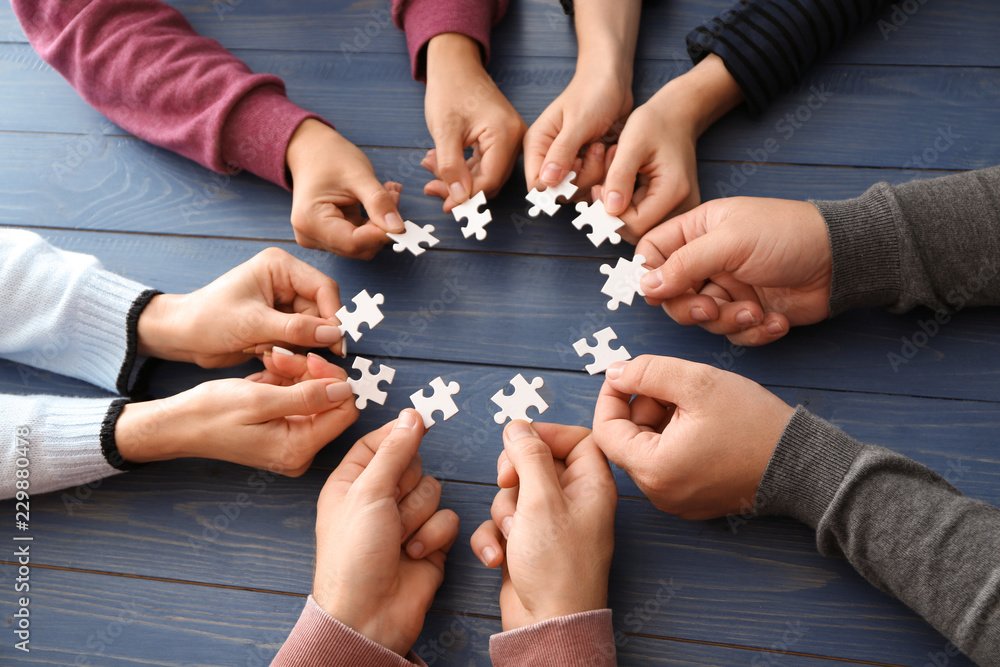 Group of people holding pieces of puzzle over wooden table Group of people holding pieces of puzzle over wooden table