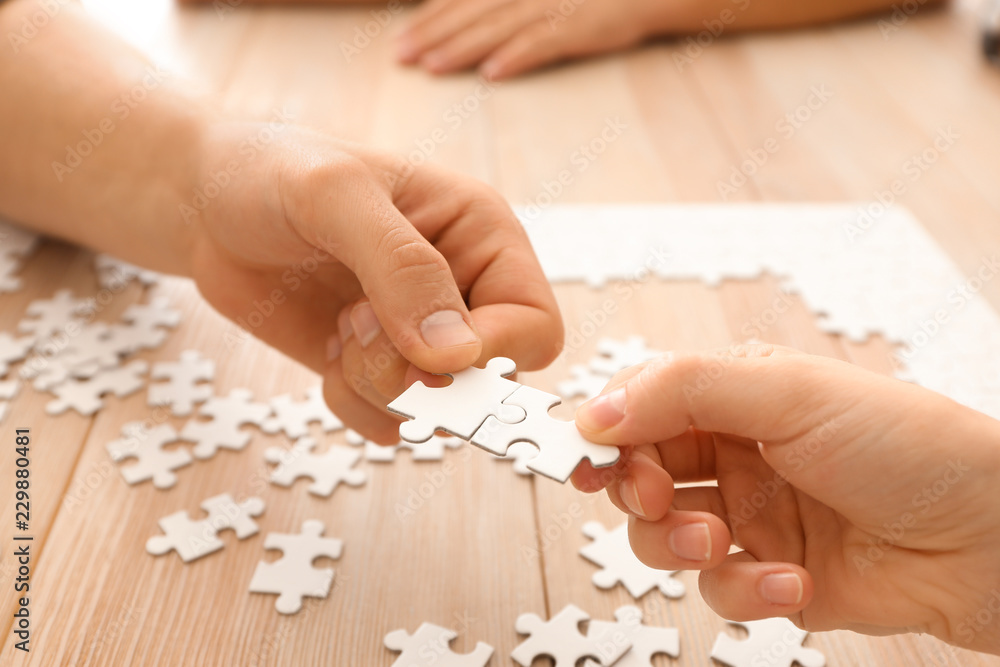 Young people assembling puzzle on wooden table