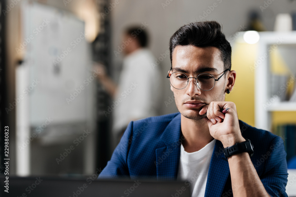 Professional young architect in glasses dressed in blue checkered jacket works on the laptop in the office Professional young architect in glasses dressed in blue checkered jacket works on the laptop in the office