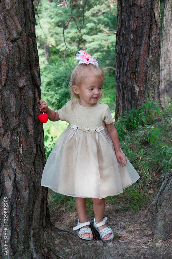 Little beautiful girl playing in nature in the forest. Standing under a tree, in the hands of a heart Little beautiful girl playing in nature in the forest. Standing under a tree, in the hands of a heart