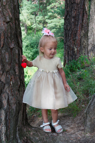 Little beautiful girl playing in nature in the forest. Standing under a tree, in the hands of a heart