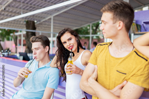 A company of good-looking friends laughing  drinking yellow cocktails and socialising at the bar in the nice summer cafe. Cheers. Entertainment  having good time. Friendship.