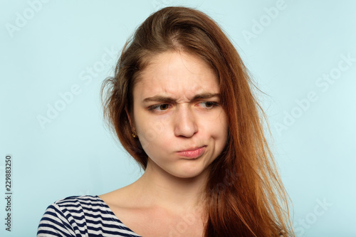 displeased capricious moody huffy girl with pursed lips. young woman portrait on blue background. boyfriend problems and emotion expression concept.