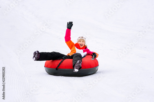 Child girl on snow tubes downhill at winter day.