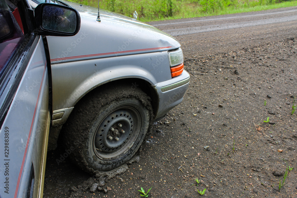 Grey van has its tires full of clay from driving on a wet clay road - 2/2 - Closeup picture on the front right wheel of the vehicle, fully surrounded by a thin layer of clay