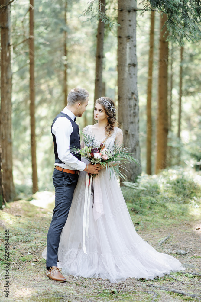 Attractive couple newlyweds, happy and joyful moment. Man and woman in festive clothes sit on the stones near the wedding decoration in boho style. Ceremony outdoors.
