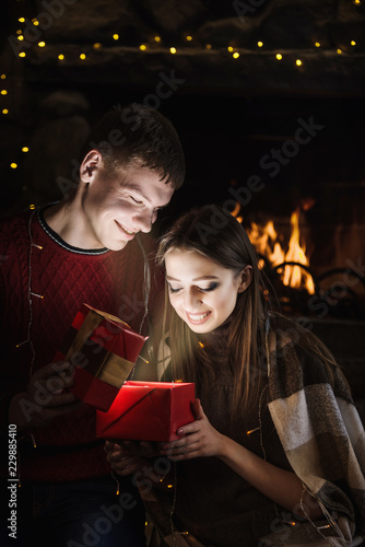 Happy young couple open gift in cozy evening near fireplace