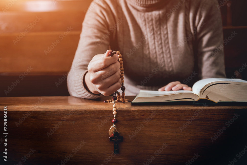 Obraz premium Christian woman praying in church. Hands crossed and Holy Bible on wooden desk.