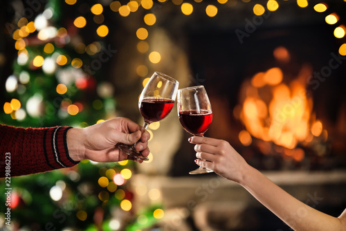 Celebrate christmas with red wine in glasses. Couple clink glasses near fireplace. Hands closeup