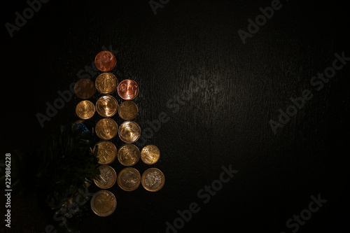 Christmas New year tree figure look like arrow symbol made of euro coins and cone pine on dark wooden background