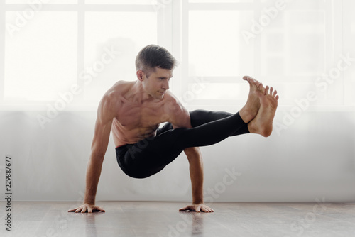 Fit muscular flexible man posing in difficult yoga pose