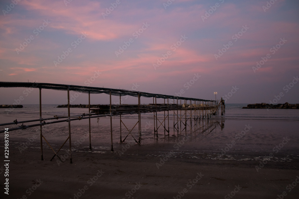 Peaceful evening on the shore, with scenic pink sunset reflected on water ant metallic pier; adriatic sea