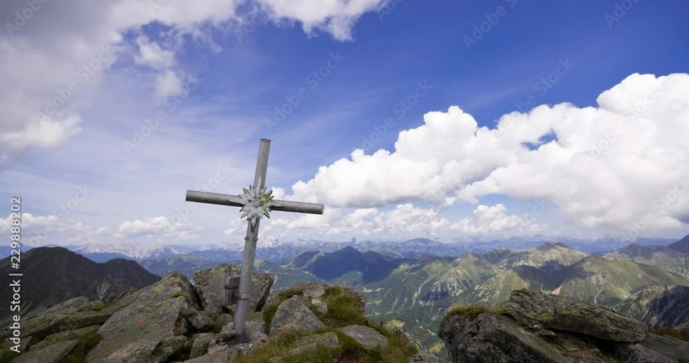 Time lapse of cloudy blue sky above leaning summit cross at Gamskogel, Triebener Tauern in Austria. Clear views over the high alpine landscape in windy weather in summer. Light and shade change. Time lapse of cloudy blue sky above leaning summit cross at Gamskogel, Triebener Tauern in Austria. Clear views over the high alpine landscape in windy weather in summer. Light and shade change.