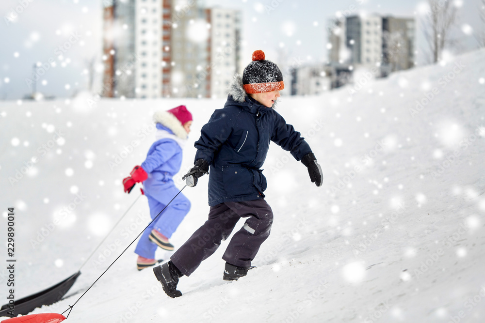 childhood, sledging and season concept - happy little kids with sleds climbing snow hill in winter