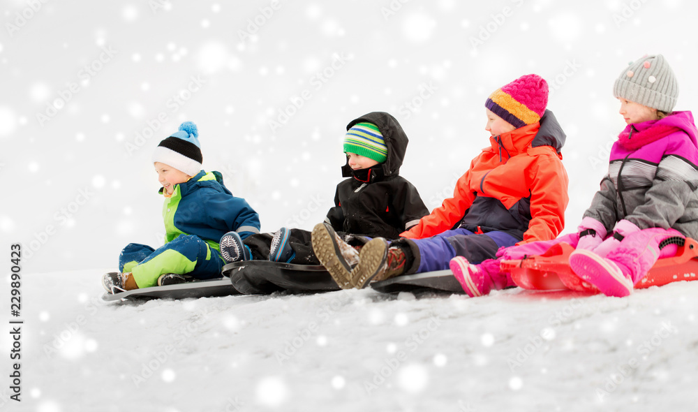 childhood, sledging and season concept - group of happy little kids sliding on sleds in winter