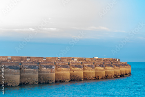 Concrete wall stretching out to sea around a marina with sunset colours