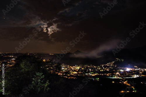 night landscape of a mountain town's lights with clouds and moon