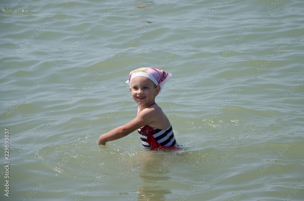Happy little charming child bathes in the sea