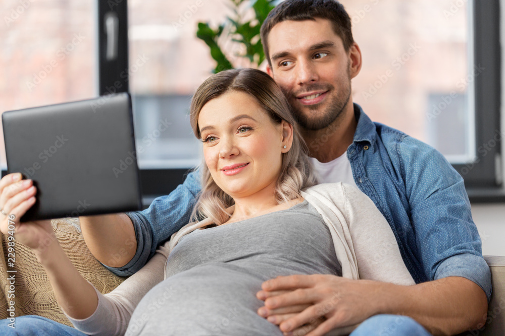 pregnancy, technology and people concept - happy man and his pregnant wife with tablet pc computer at home pregnancy, technology and people concept - happy man and his pregnant wife with tablet pc computer at home