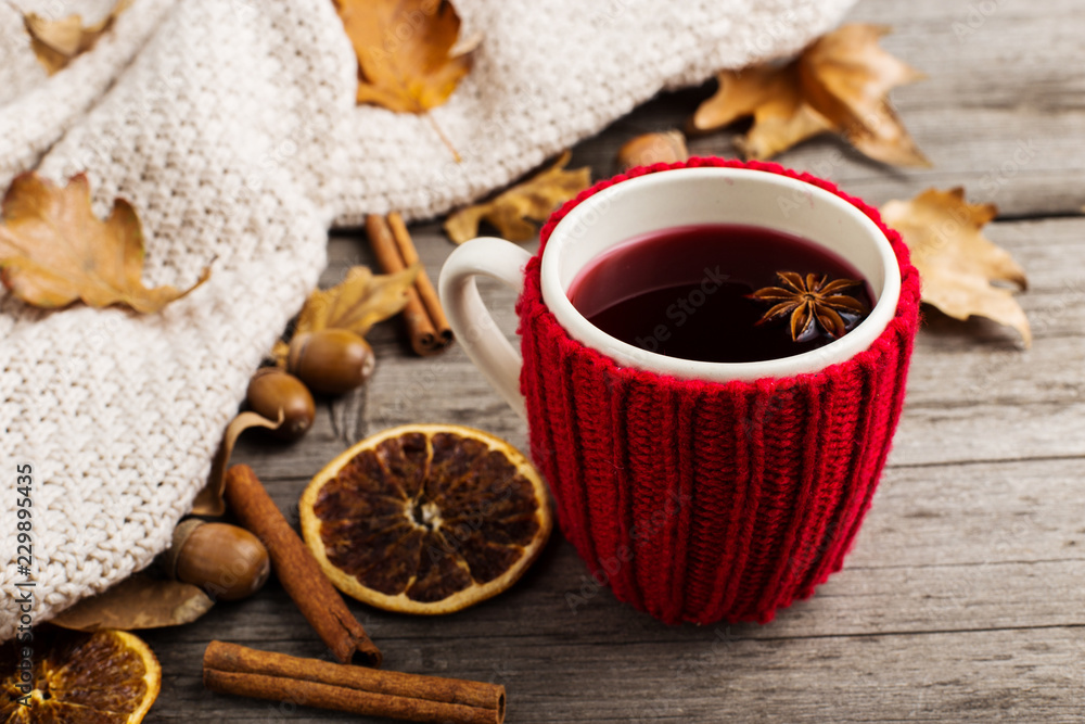 Mulled wine in a cup in a case. Leaves, knitted plaid, dry orange, cinnamon and acorns on the old wooden table, copy space, autumn. Mulled wine in a cup in a case. Leaves, knitted plaid, dry orange, cinnamon and acorns on the old wooden table, copy space, autumn.